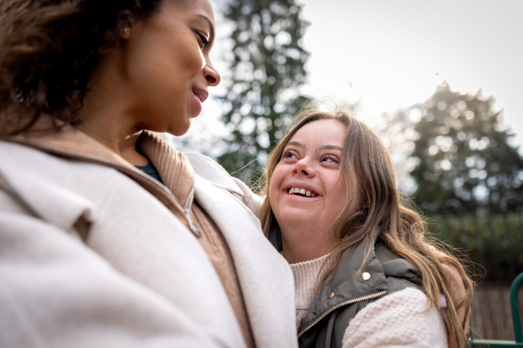Close-up of a woman with her sister who has Down syndrome smiling at each other face to face. They are both wearing warm clothing on a cold winter morning. The park is located in Gateshead.
